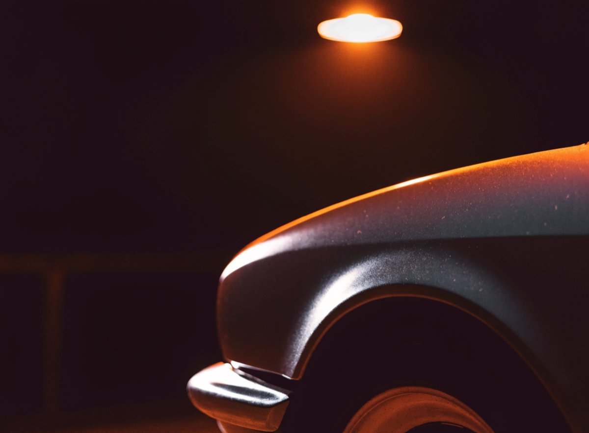 Rear haunch of a classic sports coupe under a single warm garage lamp