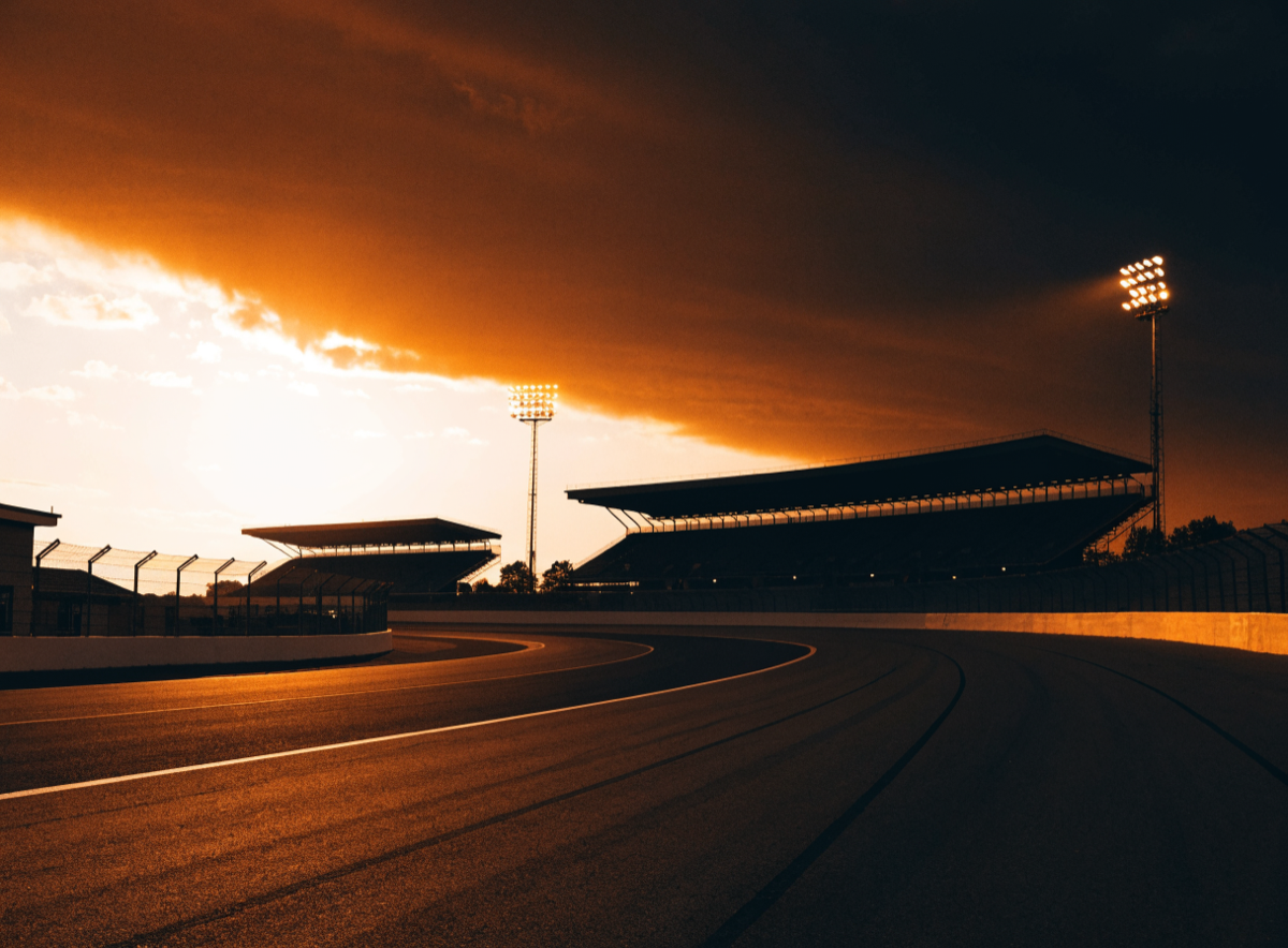 Speedway grandstands and catch fence at dusk under amber floodlights