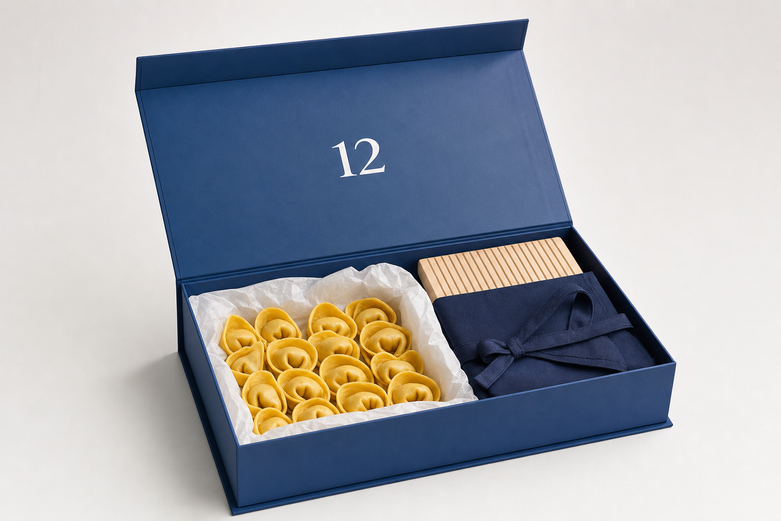 Savoy blue gift box containing fresh tortellini, a navy apron and a wooden pasta board